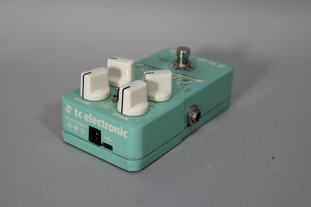A light teal pedal, angled from the front-left, with four white knobs, a toggle switch, and input/output jacks.