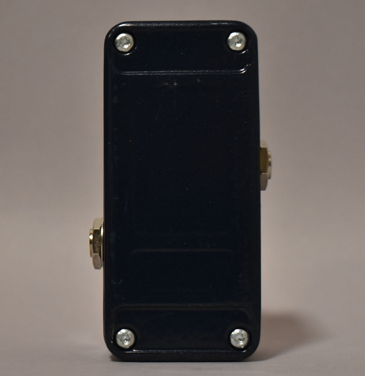 The dark blue pedal is viewed from the side, showing two silver input jacks and four silver screws on the top and bottom.
