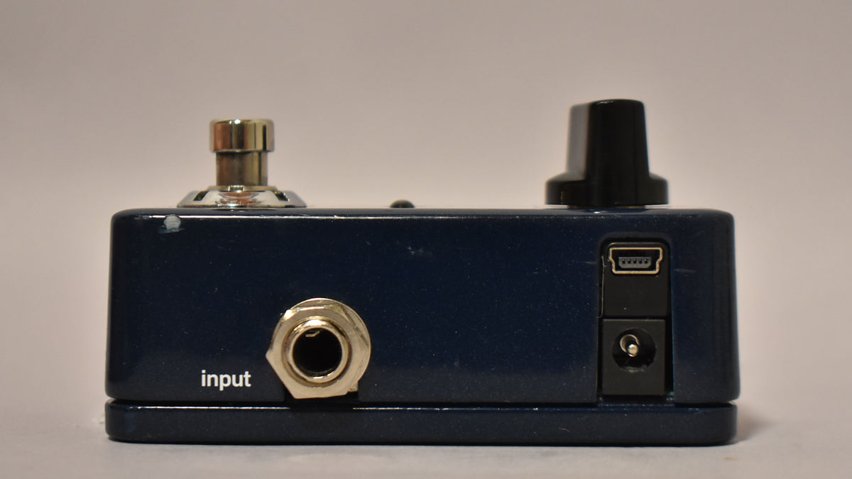 The dark blue pedal is viewed from the rear, showing the input jack, a mini-USB port, and a power input.