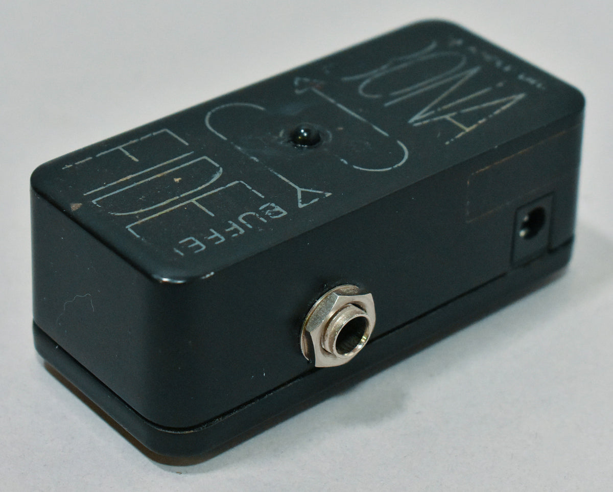 A black guitar pedal, viewed from the front-left, showing a silver input jack and a small power input on the right side.