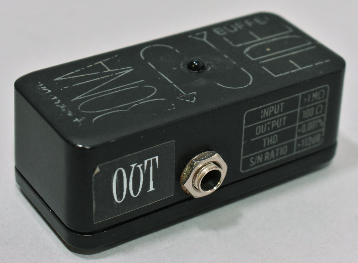 The black buffer pedal is angled from the right, showing the output jack, a small black LED, and white text with specs.