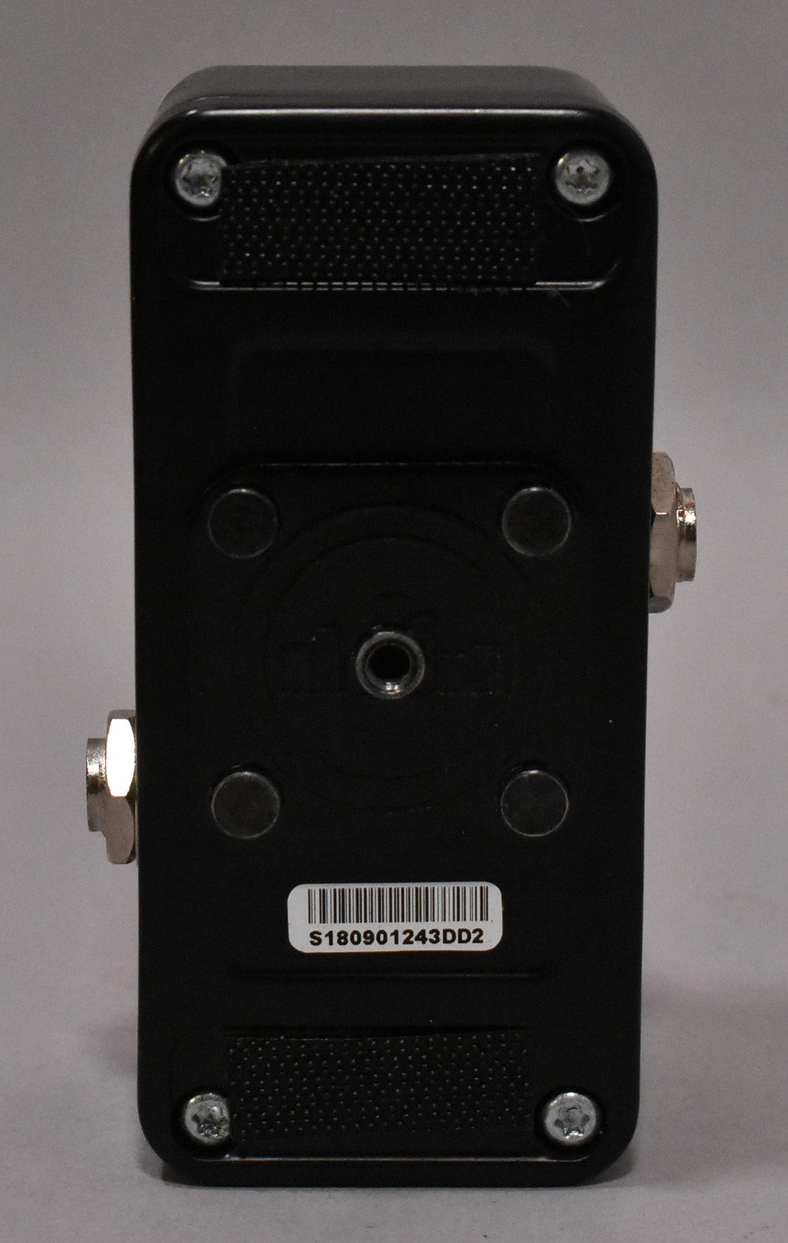 The black pedal is viewed from the bottom, showing four silver screws, a central threaded hole, and a barcode sticker.