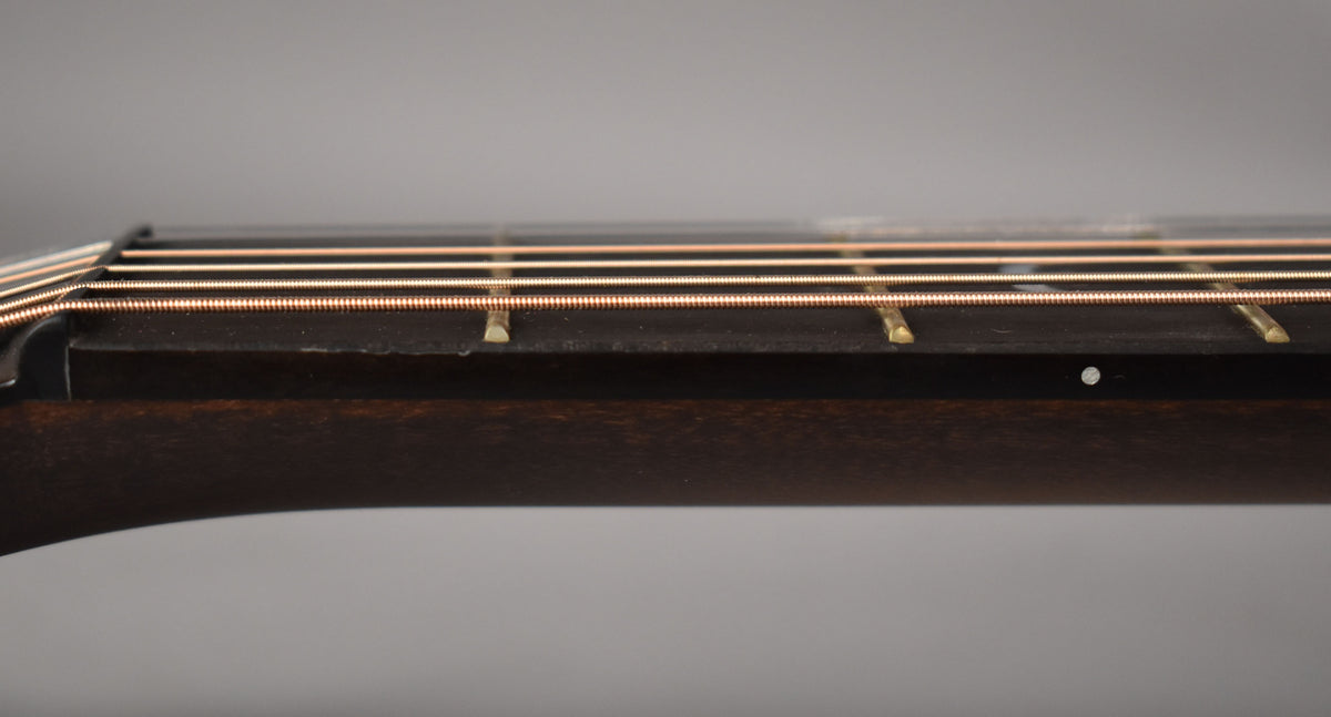 Close-up of the dark fretboard and neck from the side, showing six bronze strings and brass frets.