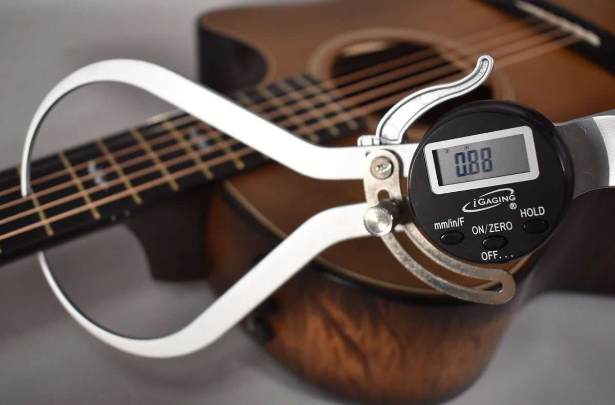 A digital caliper measures the guitar's action, showing "0.88" on its screen, with the fretboard and body blurred behind.
