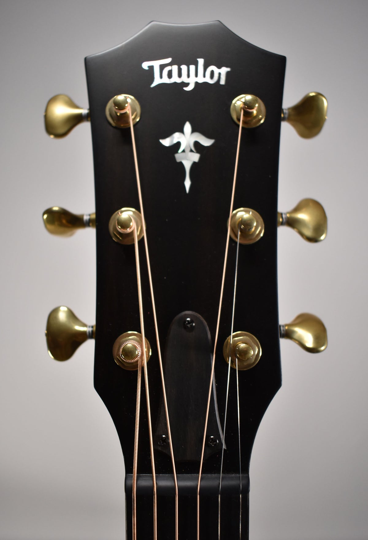 Close-up of the guitar's black headstock with gold tuners and a mother-of-pearl fleur-de-lis inlay.