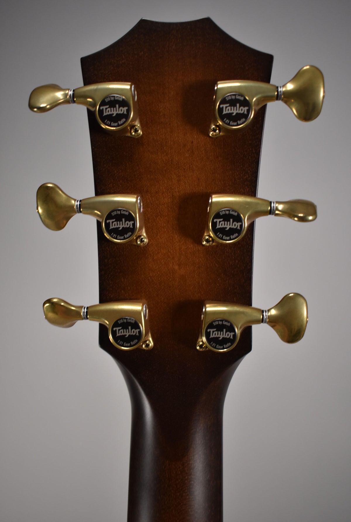 The back of the guitar's headstock and neck, showing six gold-colored tuning machines with black buttons on a dark brown wood finish.