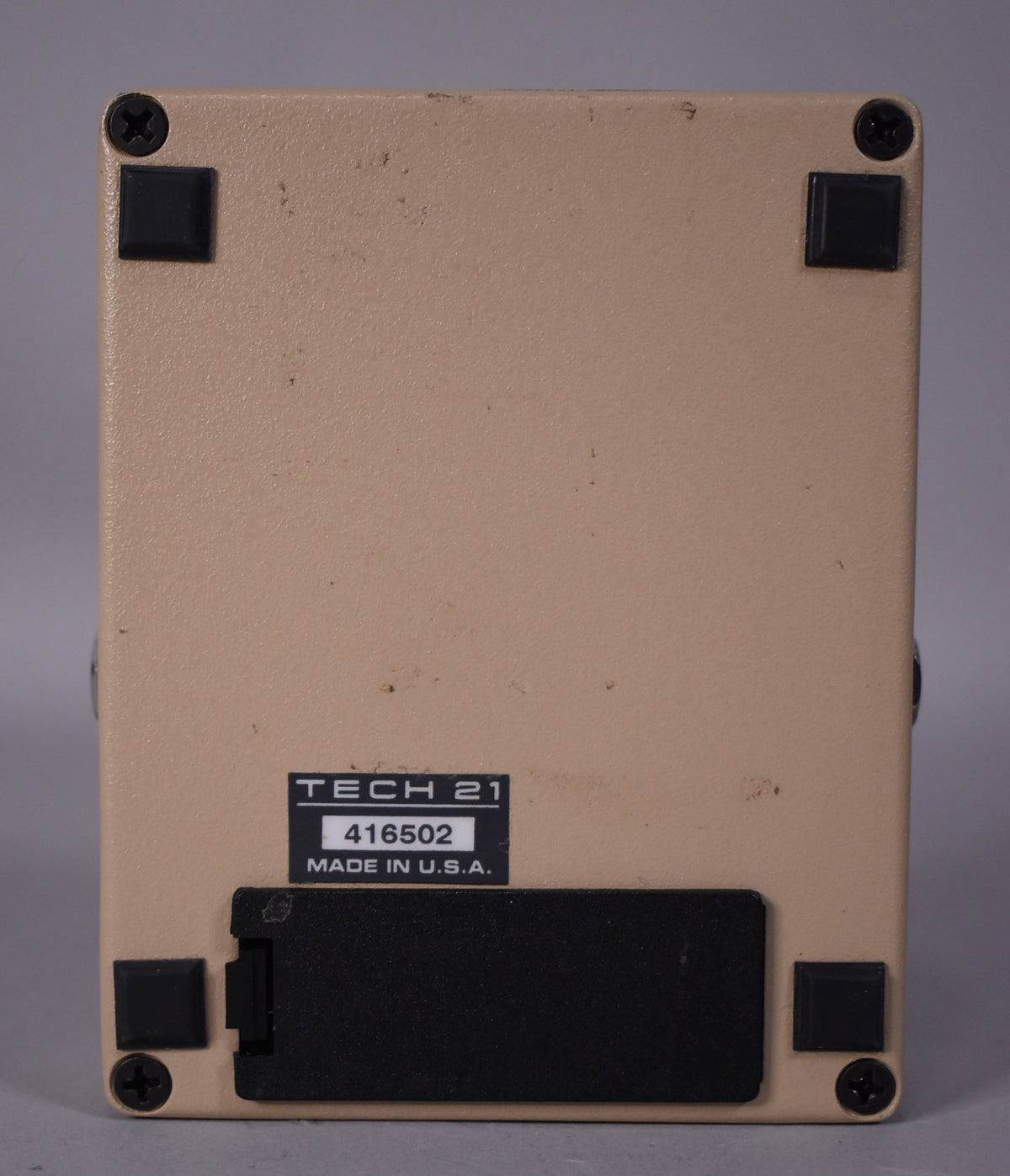 The pedal's beige underside, with four black rubber feet and screws, shows a battery compartment and a label with "TECH 21" and "MADE IN U.S.A.".
