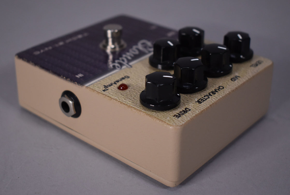 A beige pedal with a textured top, six black hexagonal knobs, a red LED, and a chrome footswitch, viewed from the front-left.