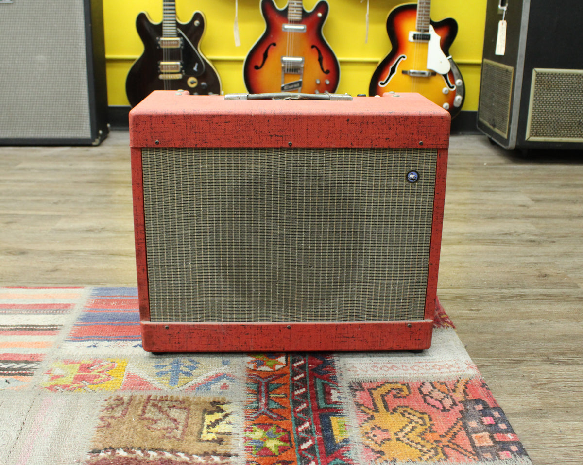 Front view of a red and black flecked tolex combo amp with a silver grille cloth, a single badge, and a top handle.