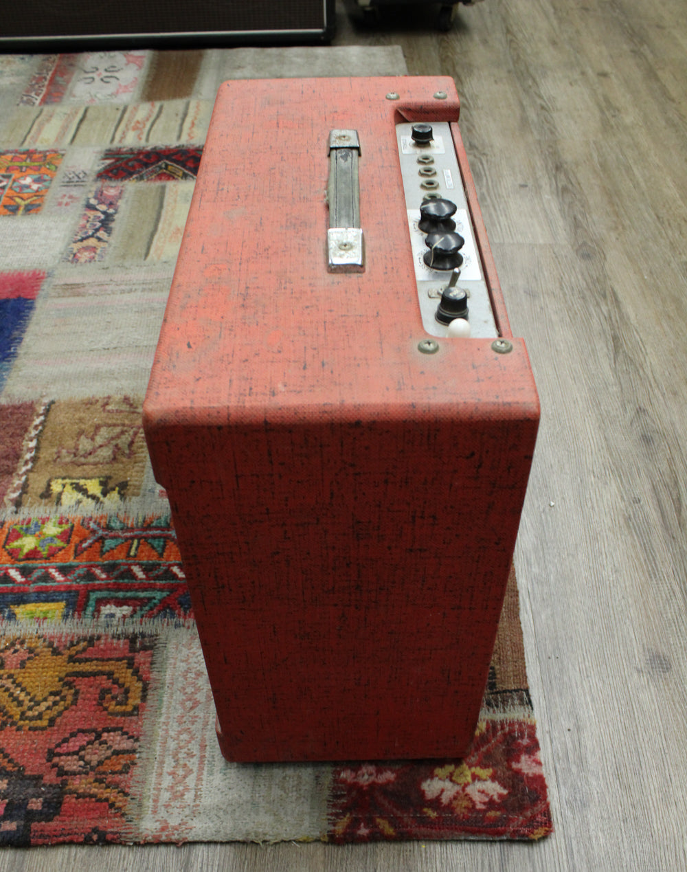 Top-down view of the red tolex amp, showing the worn metal handle and control panel with four black knobs and one white switch.