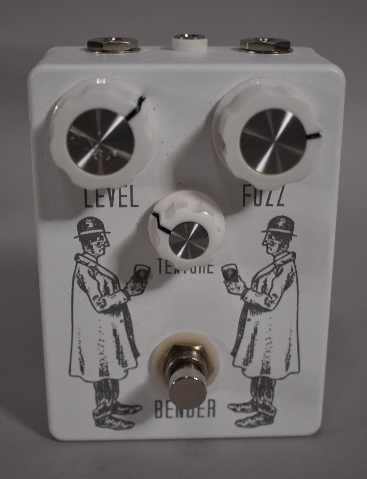 White pedal with three white knobs, a footswitch, and two black line drawings of men in trench coats and bowler hats.