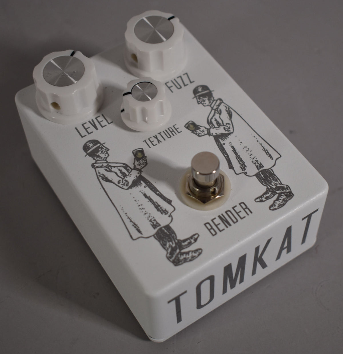 The white pedal is angled right, showing its top with three white knobs, a footswitch, and two black-inked figures.