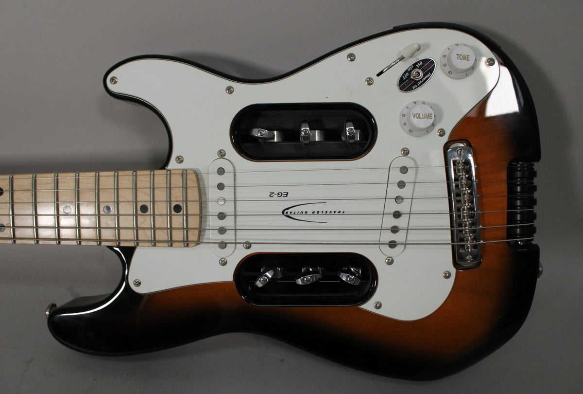 Sunburst electric guitar, angled from above, showing the body, white pickguard, maple neck, and chrome hardware.