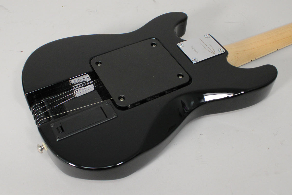 The guitar's glossy black back shows a rectangular control cavity cover, a chrome neck plate, and string-through-body ferrules.
