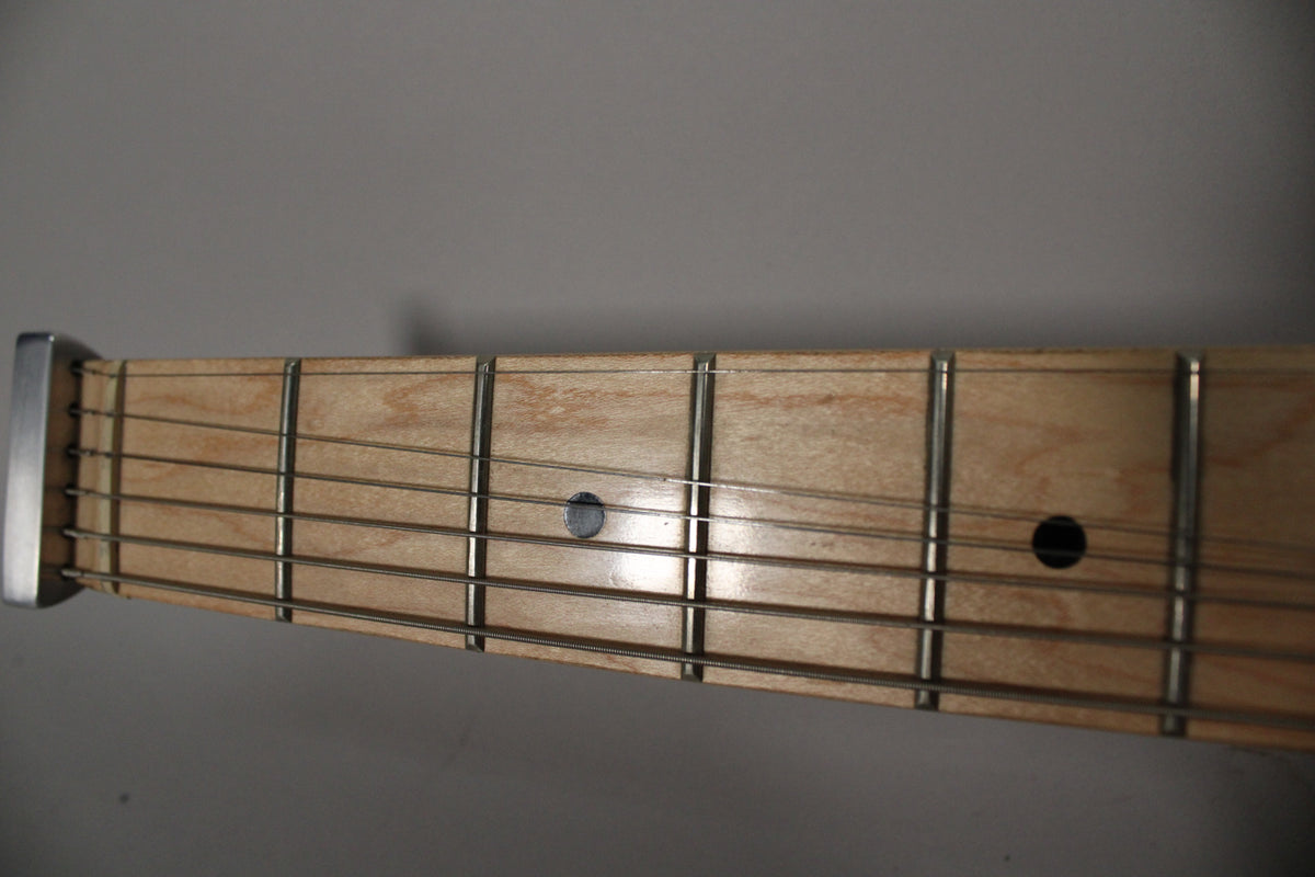 Close-up of the light wood fretboard with six strings, showing the first seven frets and two black dot inlays.