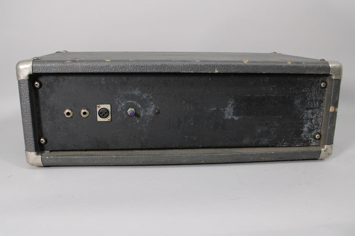 The dark gray amplifier is shown from the rear, revealing two 1/4-inch jacks, an XLR input, and a purple knob, all on a worn panel.