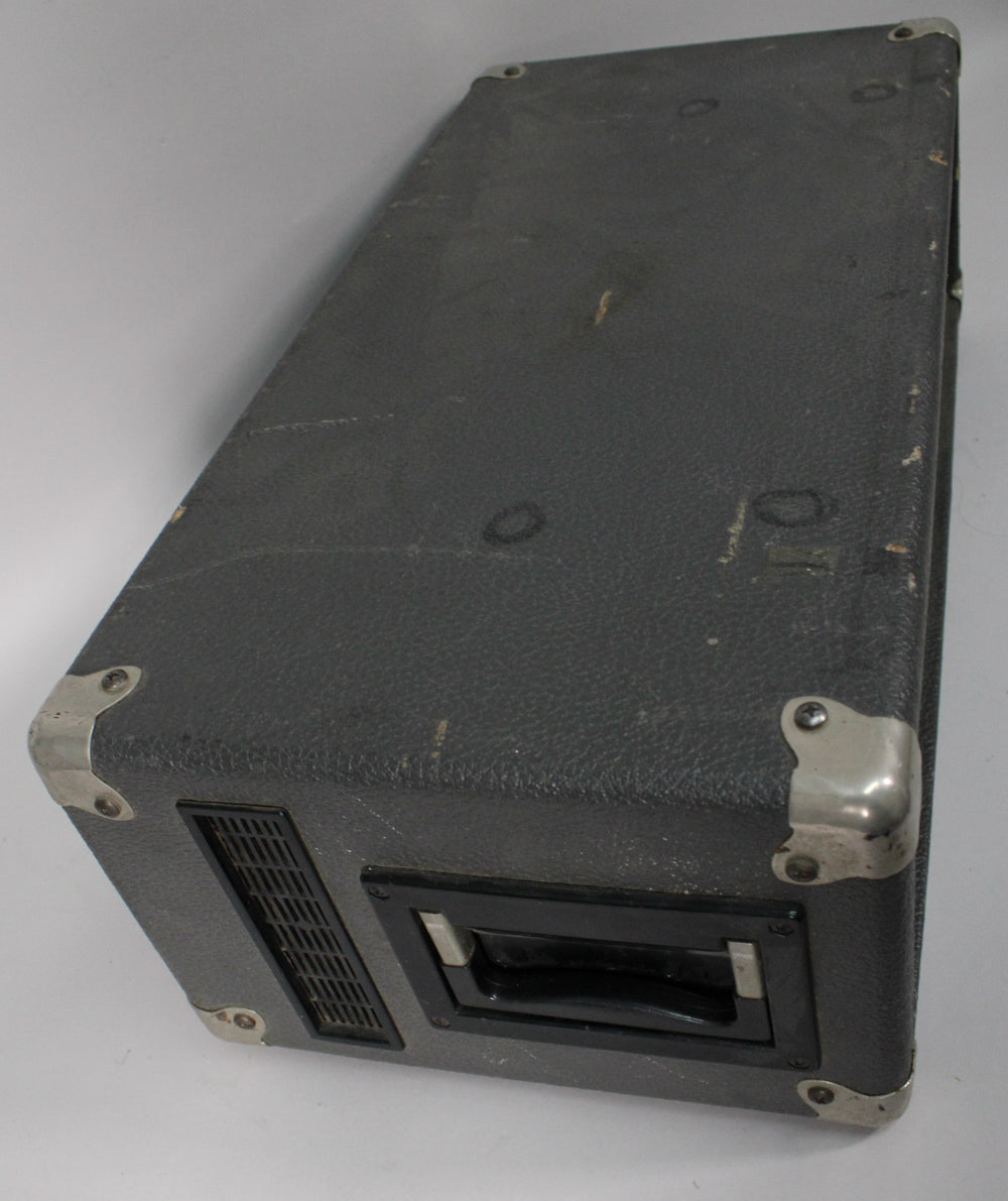 The amp's textured black casing, viewed from above, shows scuffs and wear, with a side handle and vent visible.