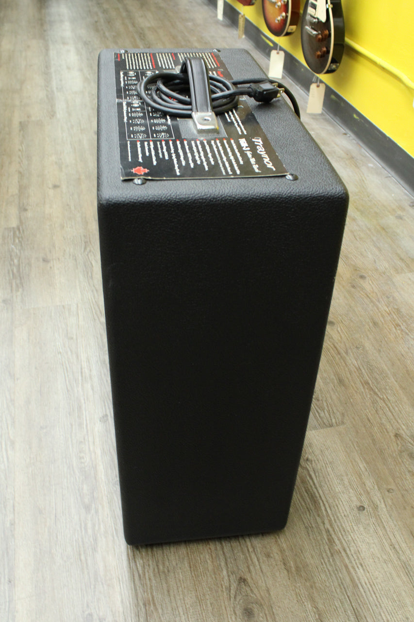 The black textured amp is viewed from above, showing its top panel with a silver handle and coiled power cable.