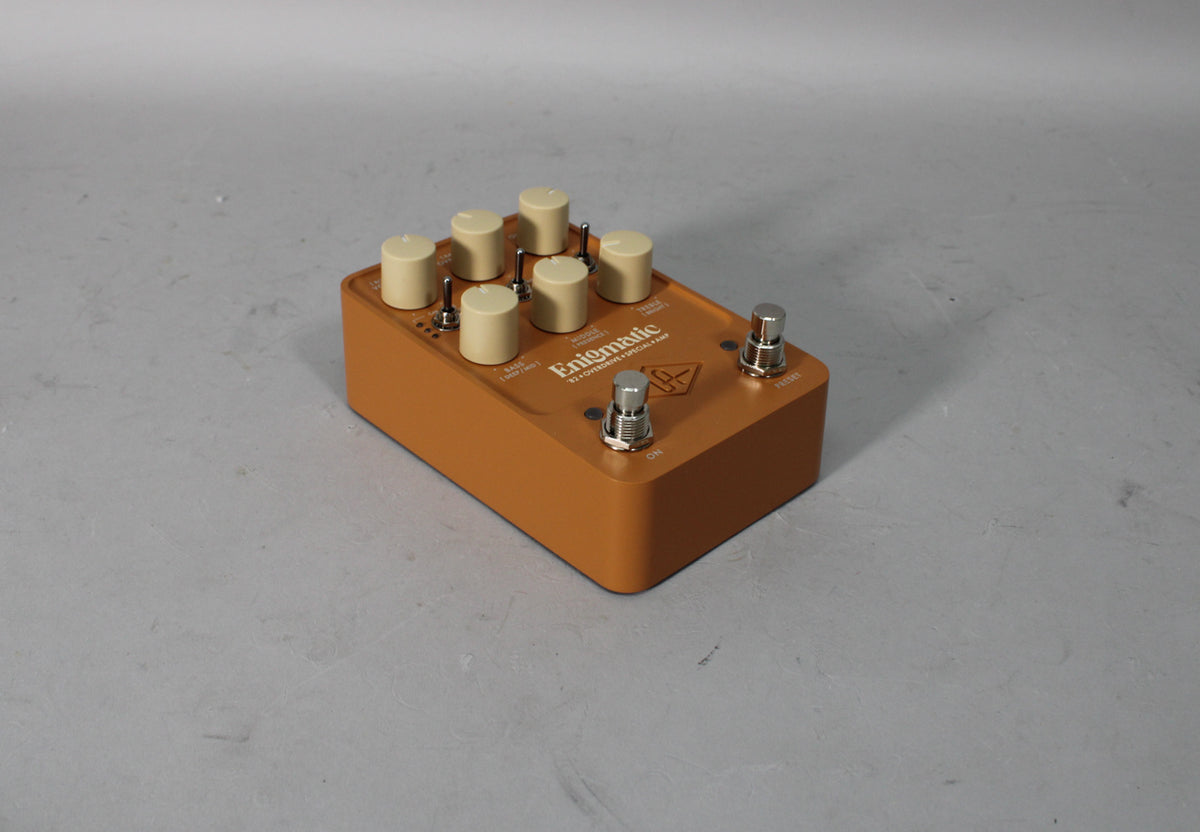 A top-down, slightly angled view of the orange pedal, showing six cream knobs, three small toggle switches, and two footswitches.