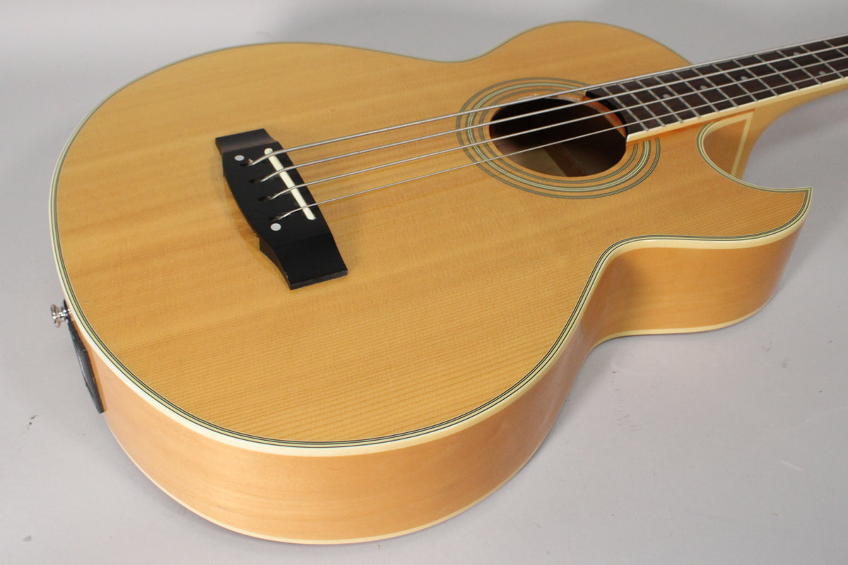 The natural finish acoustic bass is angled from the lower bout, showing the soundhole, black bridge, and cutaway.