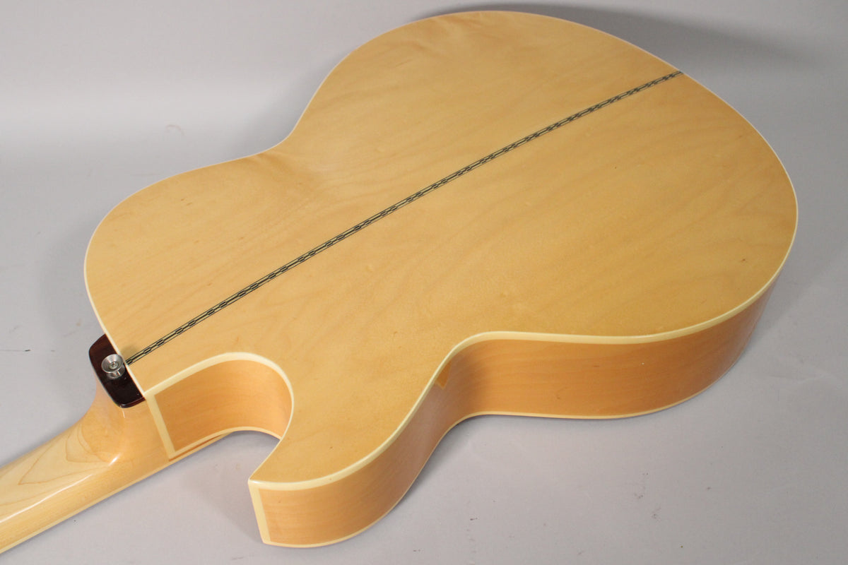 The back of the natural finish acoustic bass, showing the cutaway, neck heel, and a dark decorative stripe down the center.