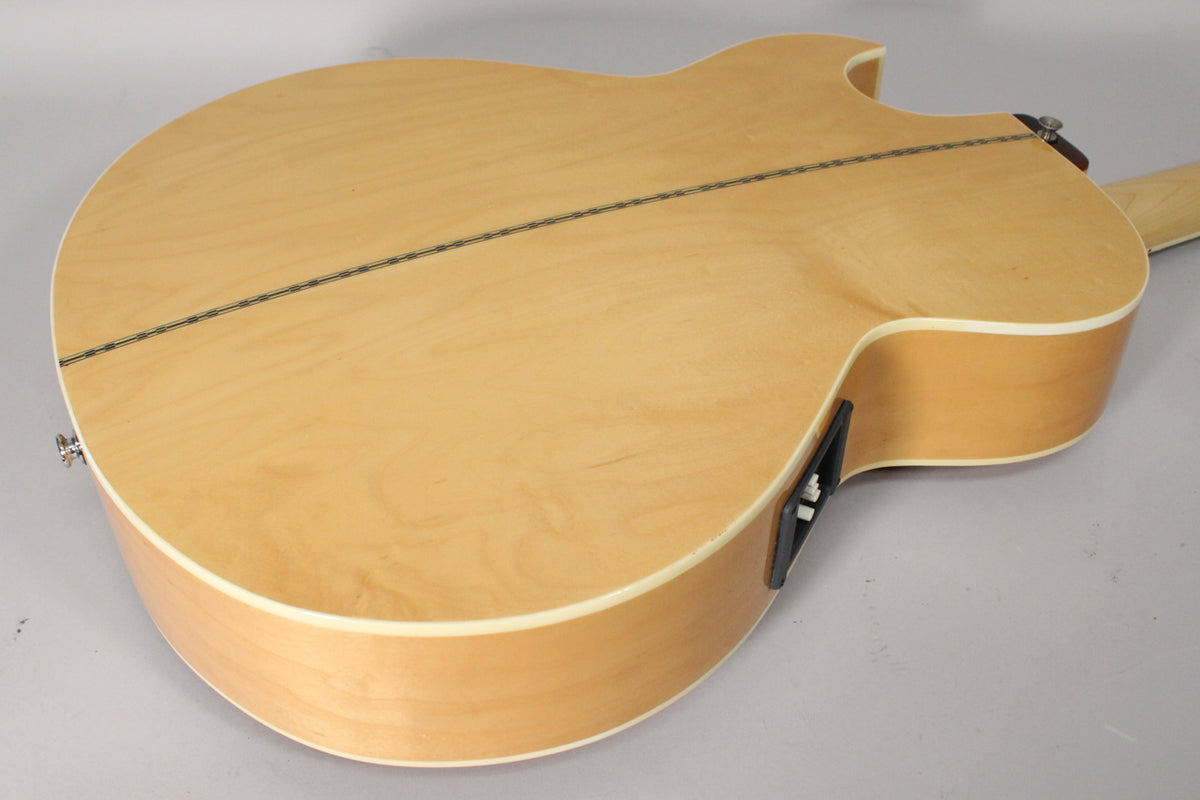 The natural finish acoustic bass body is angled, showing the light wood back with a dark center stripe and a black preamp control panel.