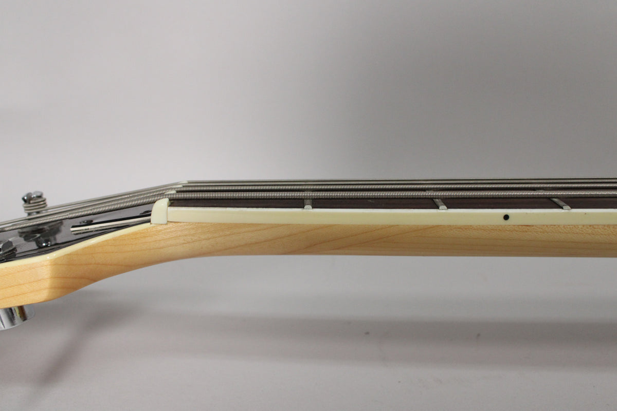Close-up of the bass neck from the side, showing the light wood, dark fretboard, white nut, and four strings.