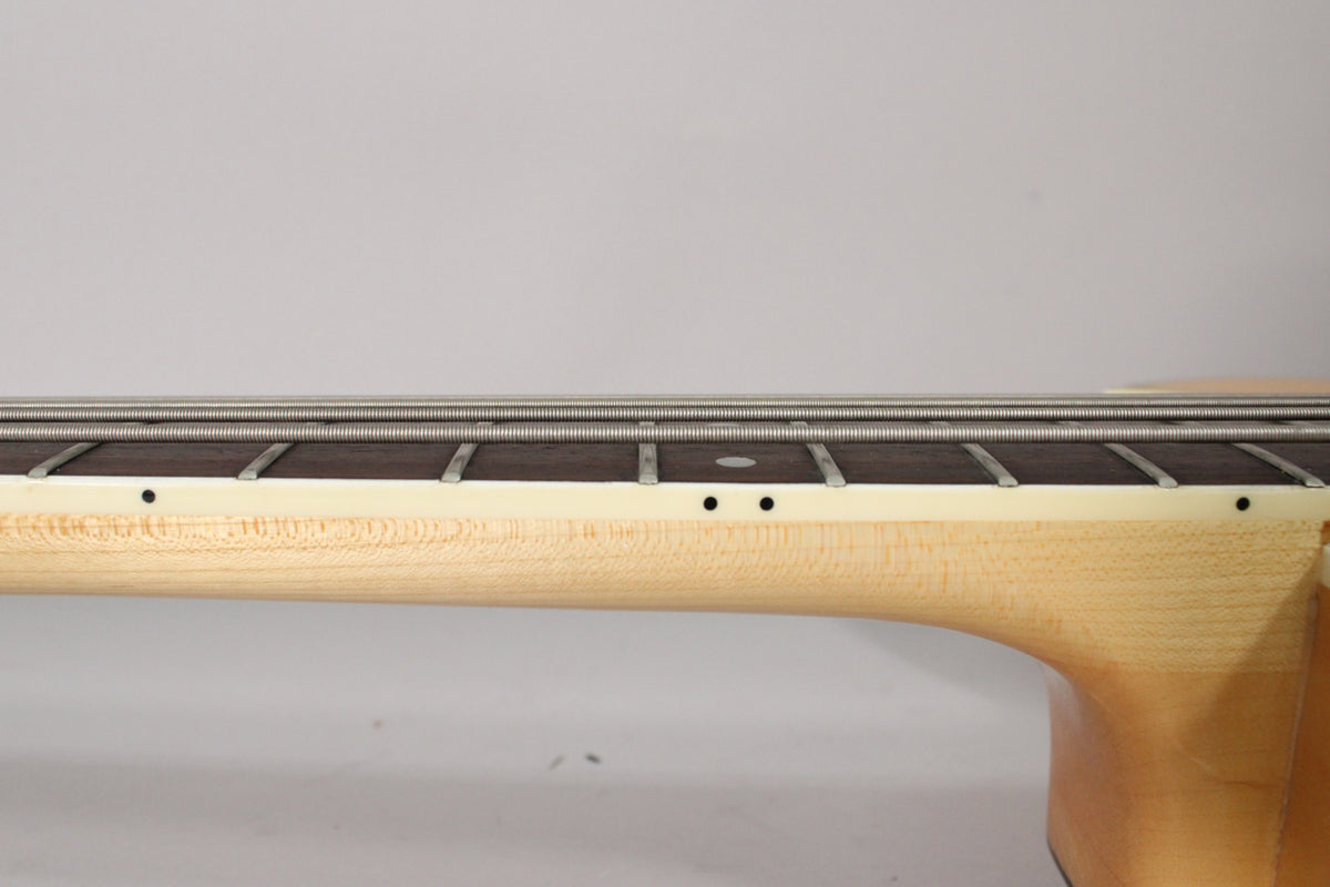 Close-up of the bass's natural maple neck and dark fretboard with four strings, showing side dot markers and light fret wear.
