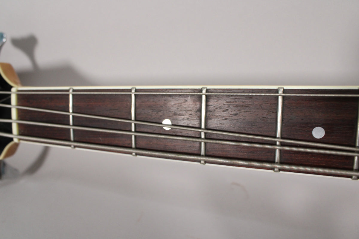 Close-up of the dark wood fretboard with four strings, showing white dot inlays and light wear on the frets.