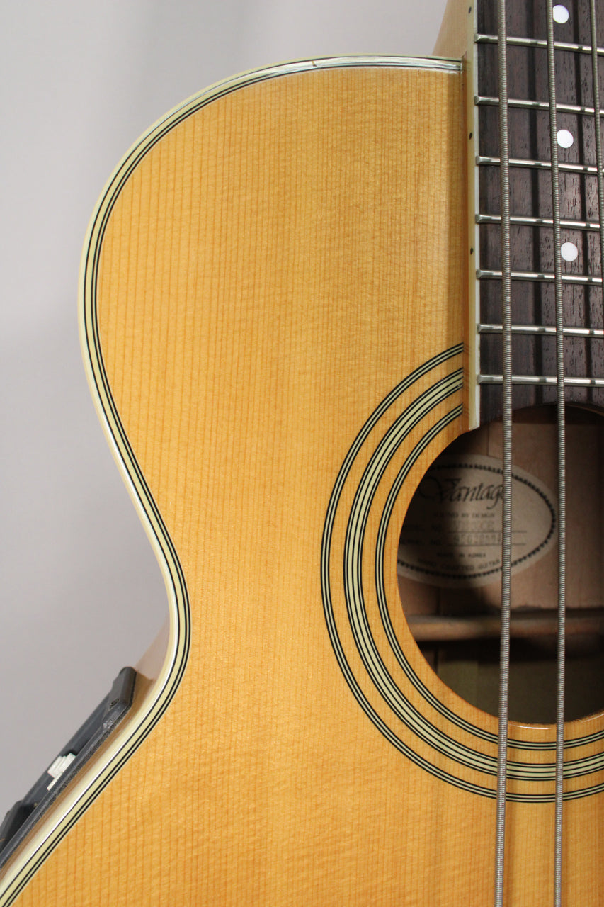 Close-up of the natural finish acoustic bass body, showing the soundhole rosette, cutaway, and part of the dark fretboard.