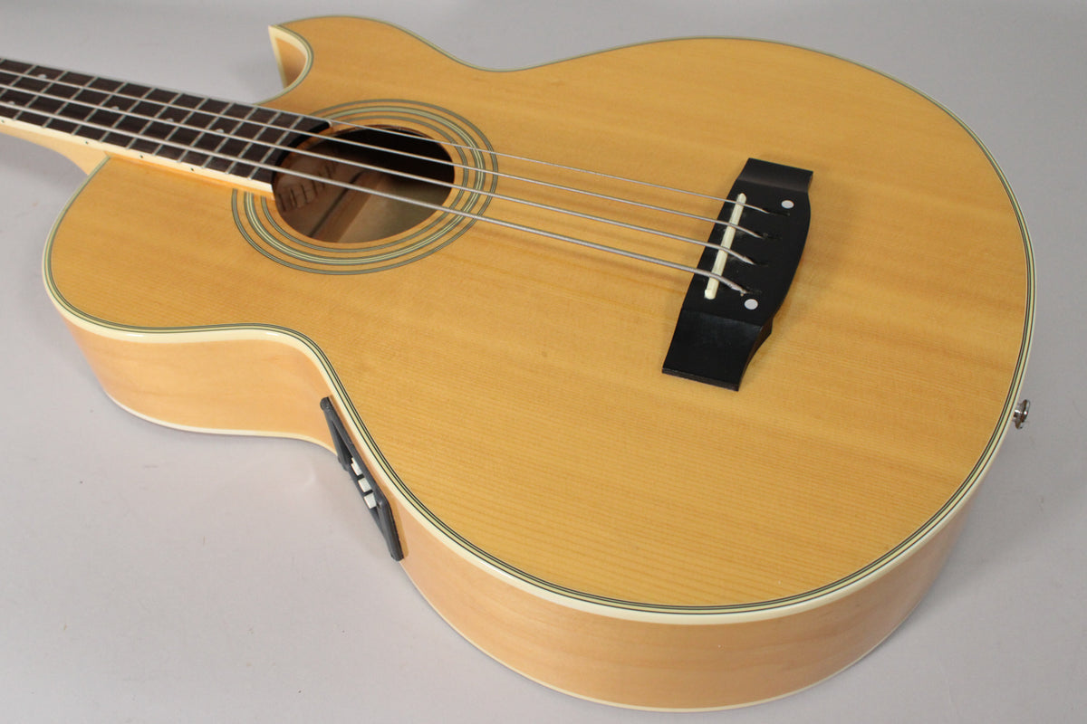 The natural finish acoustic bass is angled from the upper left, showing the light wood body, soundhole, and black bridge.