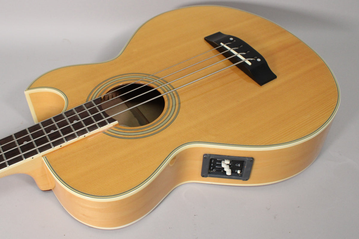 The natural finish acoustic bass is angled, showing its light wood body, dark fretboard, soundhole, bridge, and side-mounted preamp.