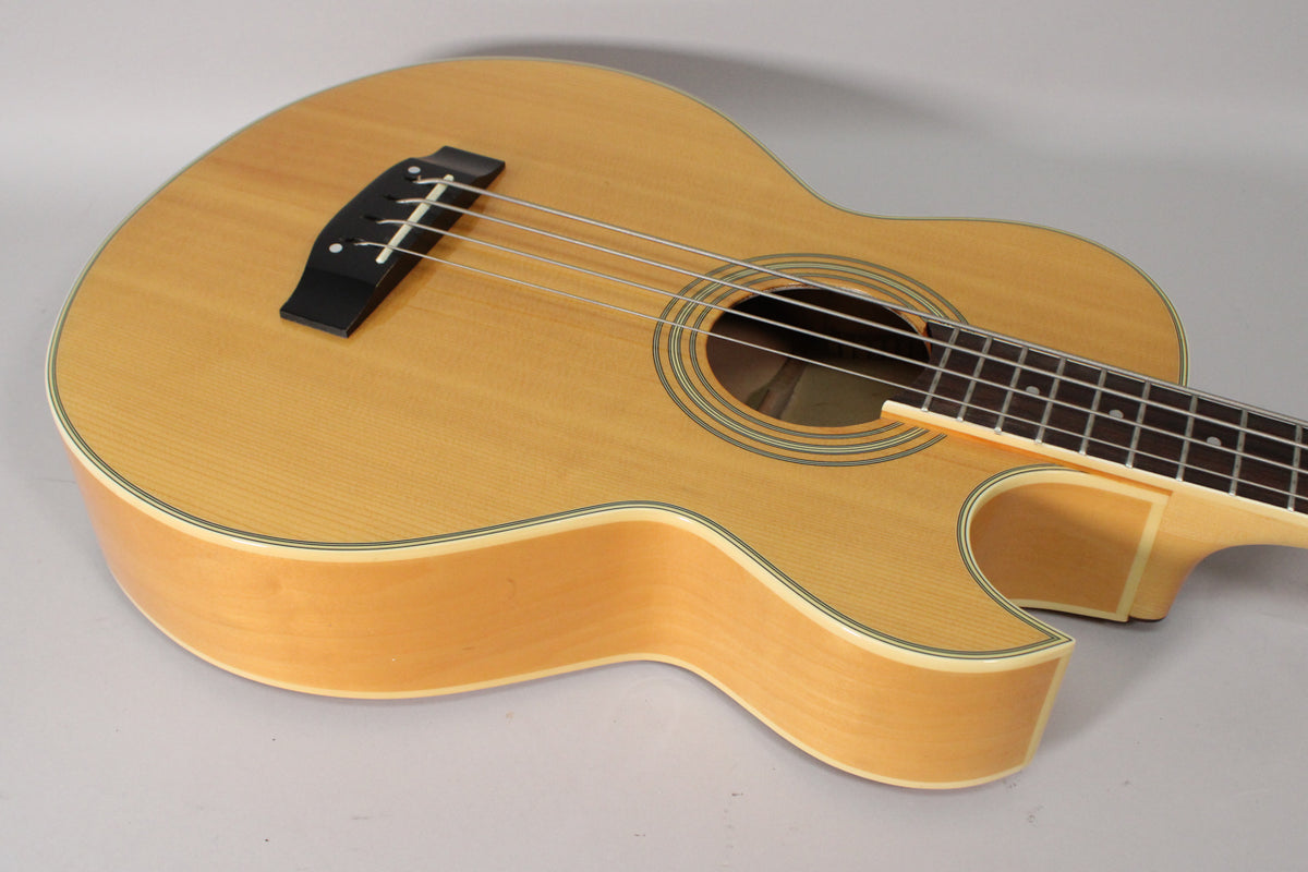 The natural finish acoustic bass is angled from the upper left, showing the light wood body, soundhole, and dark fretboard.