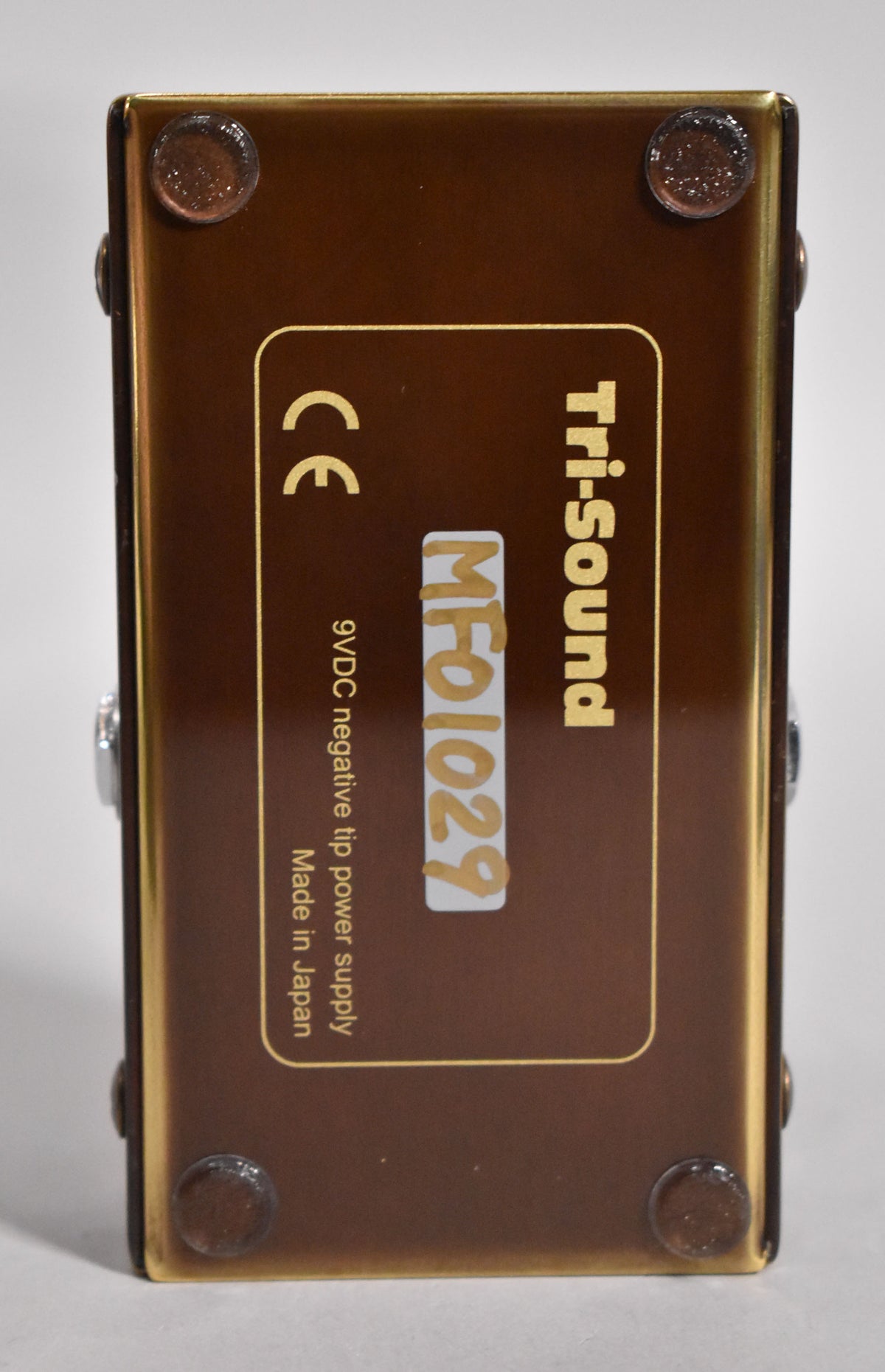 The pedal's brown base is shown from above, with four clear rubber feet and a white sticker with "MF01029" in orange.