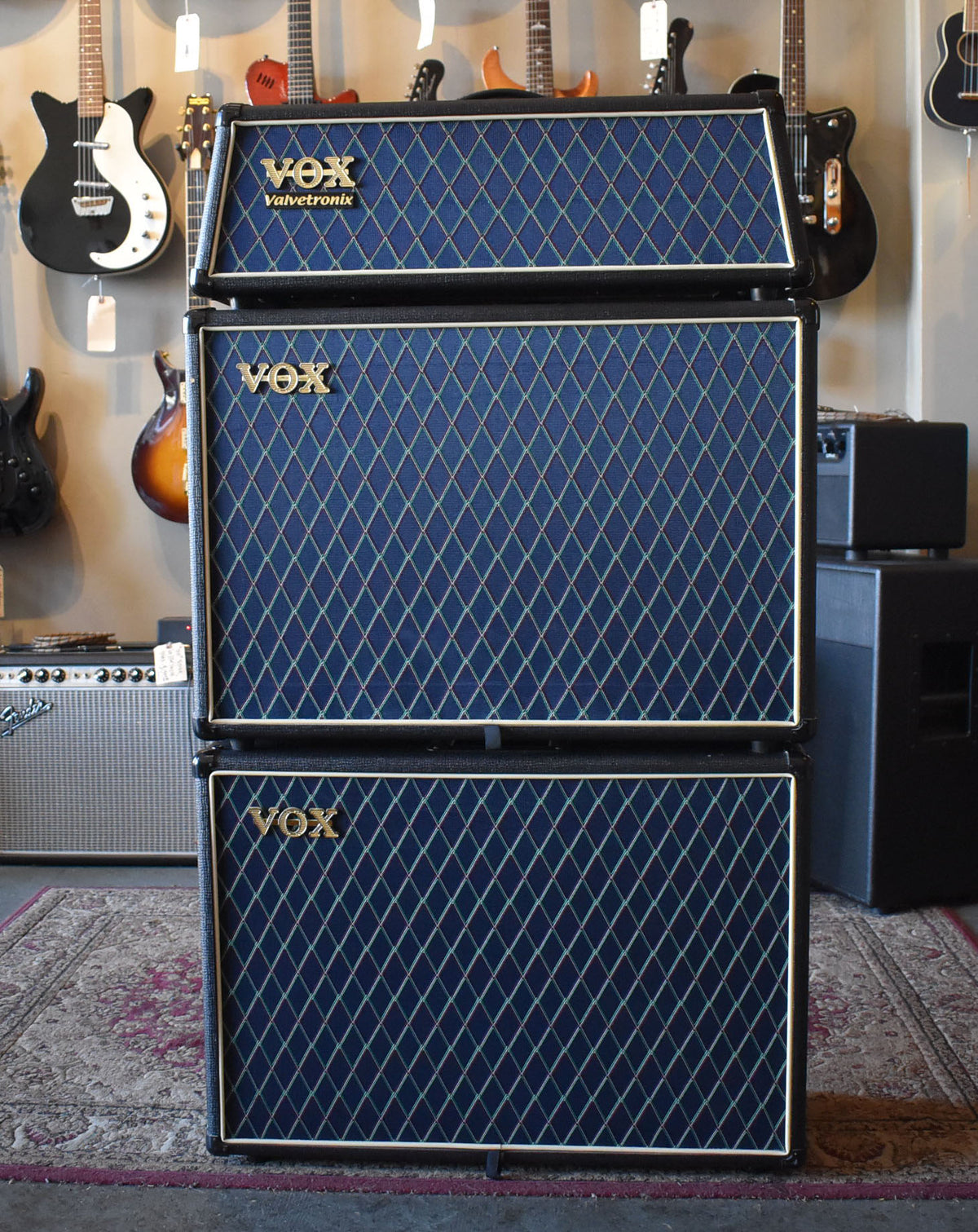 Full front view of a black amp head atop two matching cabinets, all with dark blue diamond-patterned grille cloth.