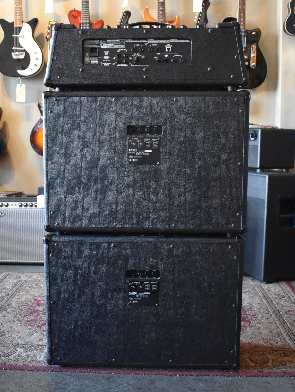 Rear view of a black textured amplifier head stacked on two matching speaker cabinets, showing various input/output jacks.