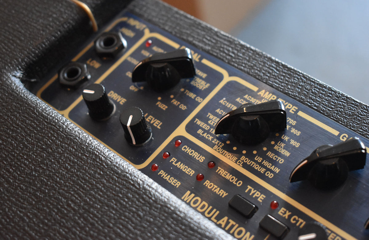 Close-up of the amp's black control panel with gold trim, showing black knobs, input jacks, and red indicator lights.