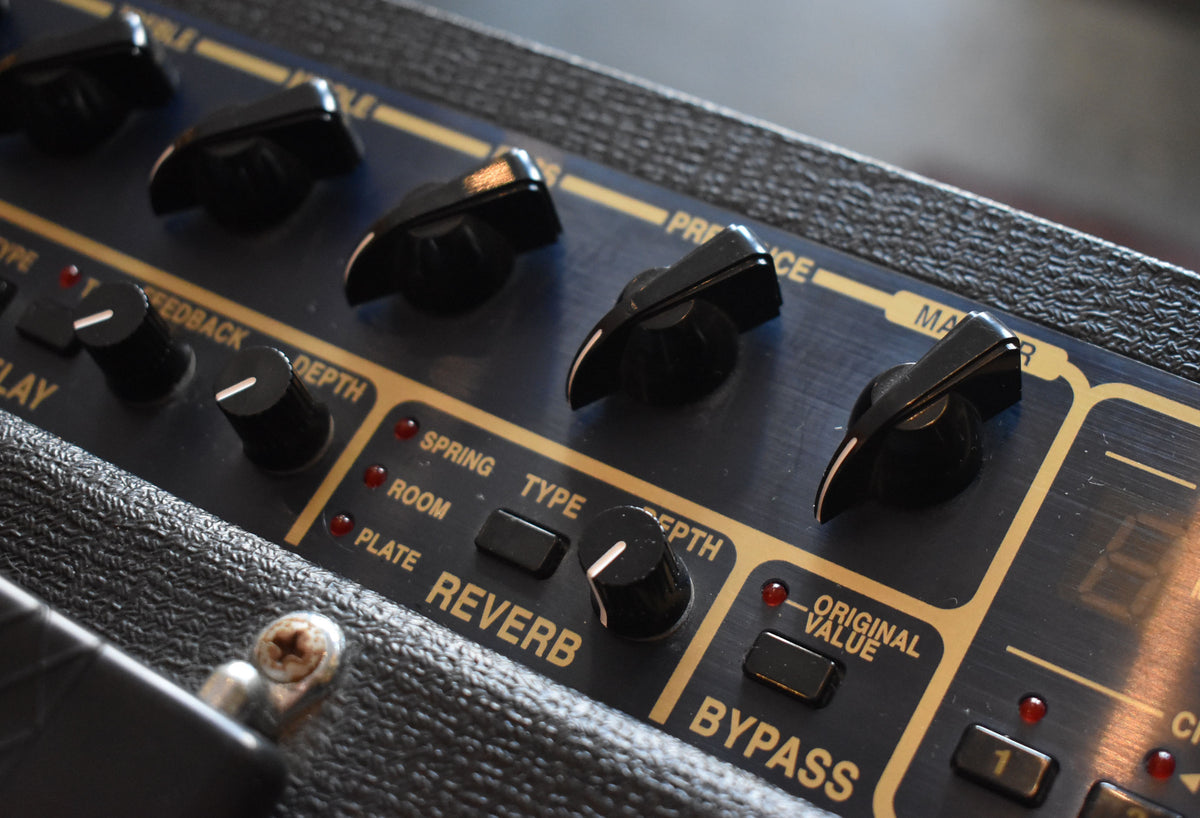 Close-up, angled view of the amp's dark blue control panel with gold accents, showing black knobs, buttons, and red indicator lights.