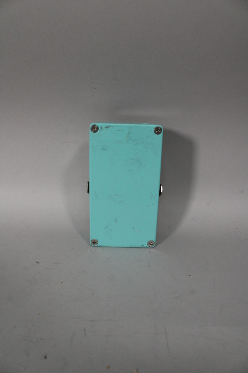 The teal pedal is viewed from the back, showing its four silver screws and two side jacks, with some scuffs and scratches.