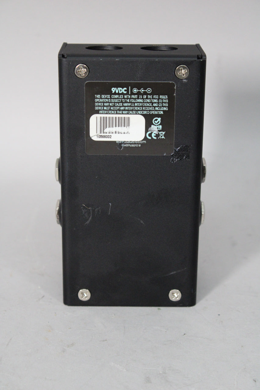 The black pedal is viewed from the rear, showing the input/output jacks, power input, and a product information sticker.