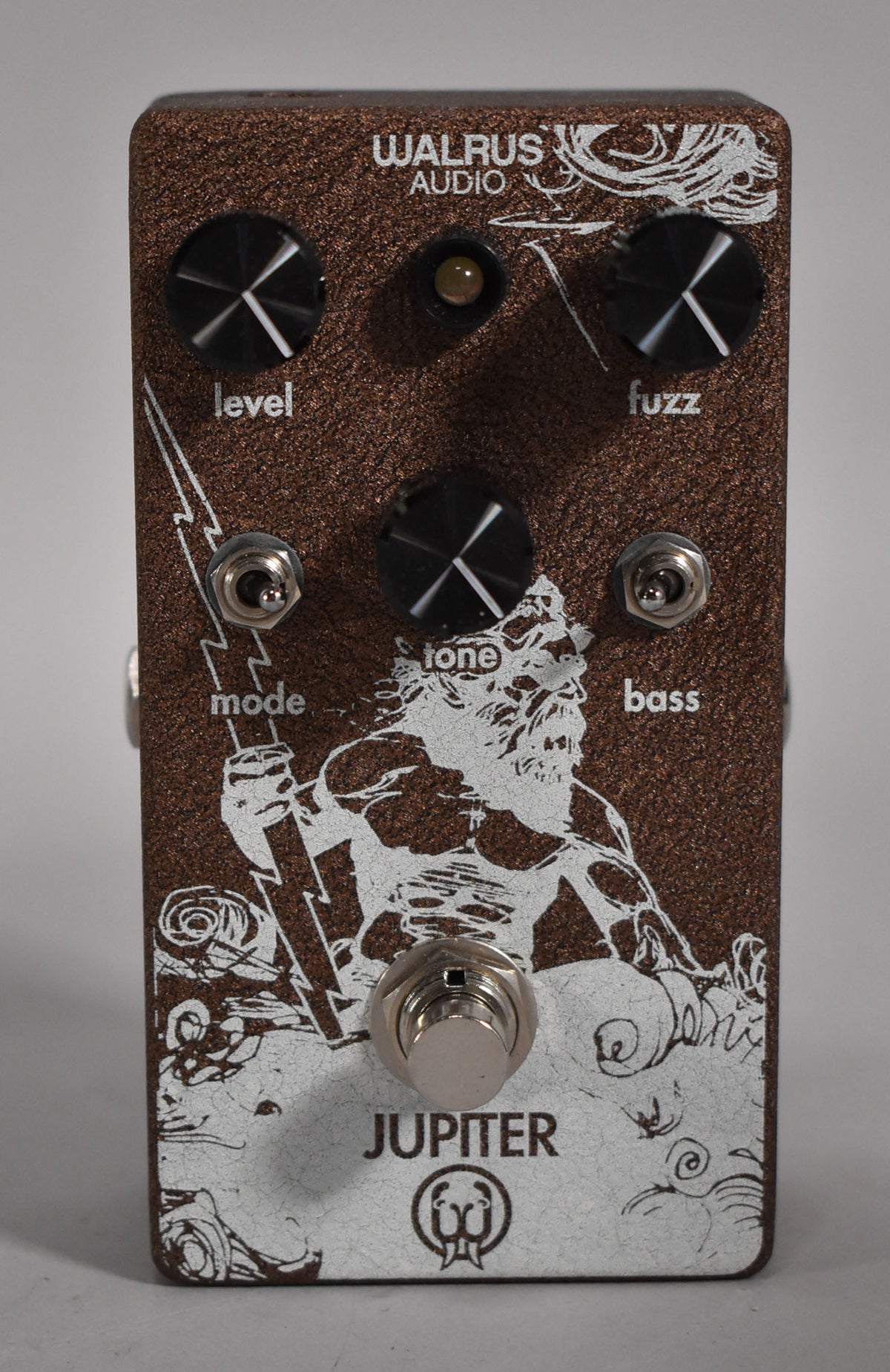 A top-down view of a brown textured pedal with white Zeus graphic, three black knobs, two toggle switches, and a footswitch.
