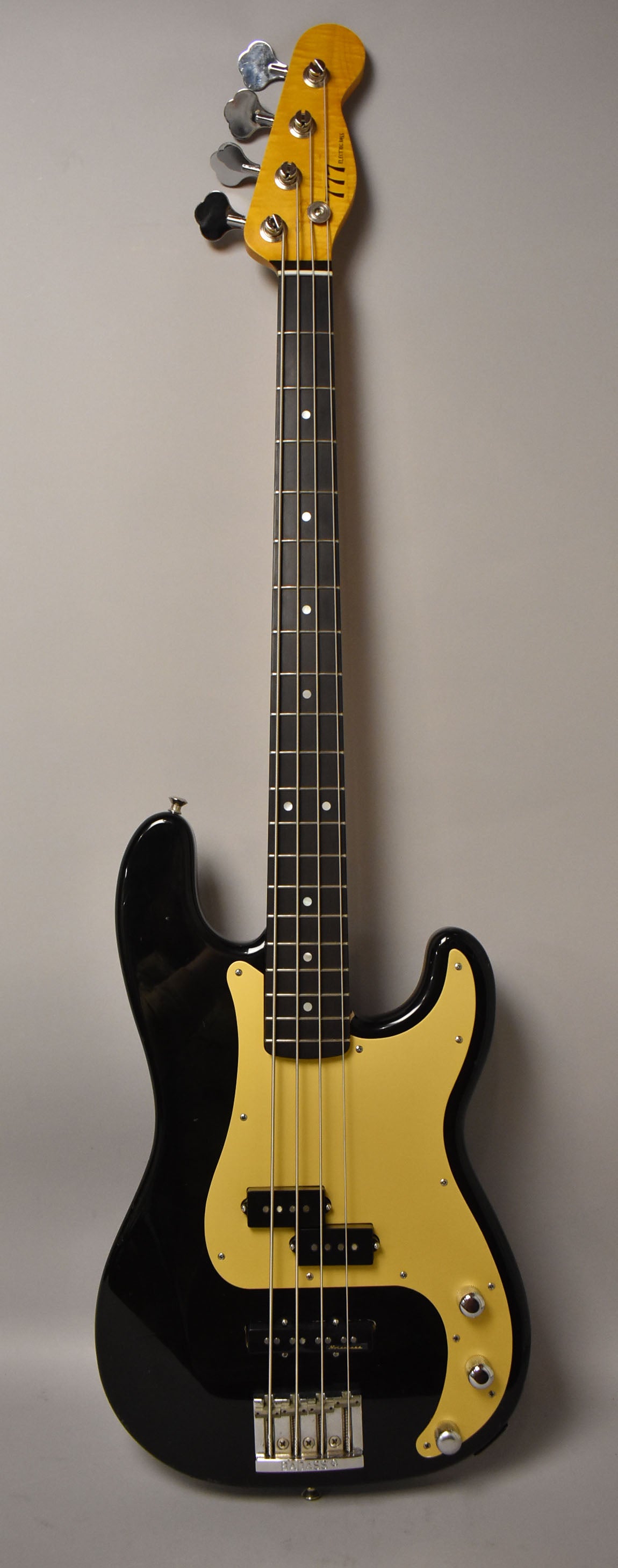 Full view of a black bass with a glossy finish, a maple neck, dark fretboard, and a large gold pickguard.