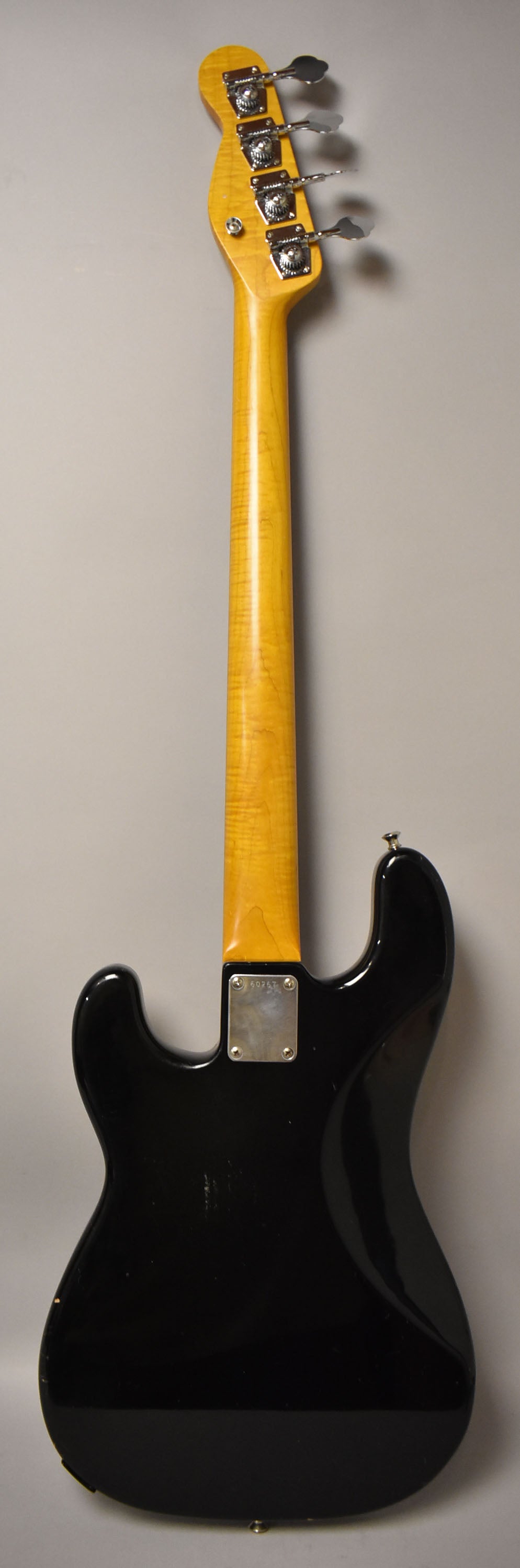 Full rear view of a black bass with a glossy finish and a maple neck, showing some scratches on the body and a chrome neck plate.