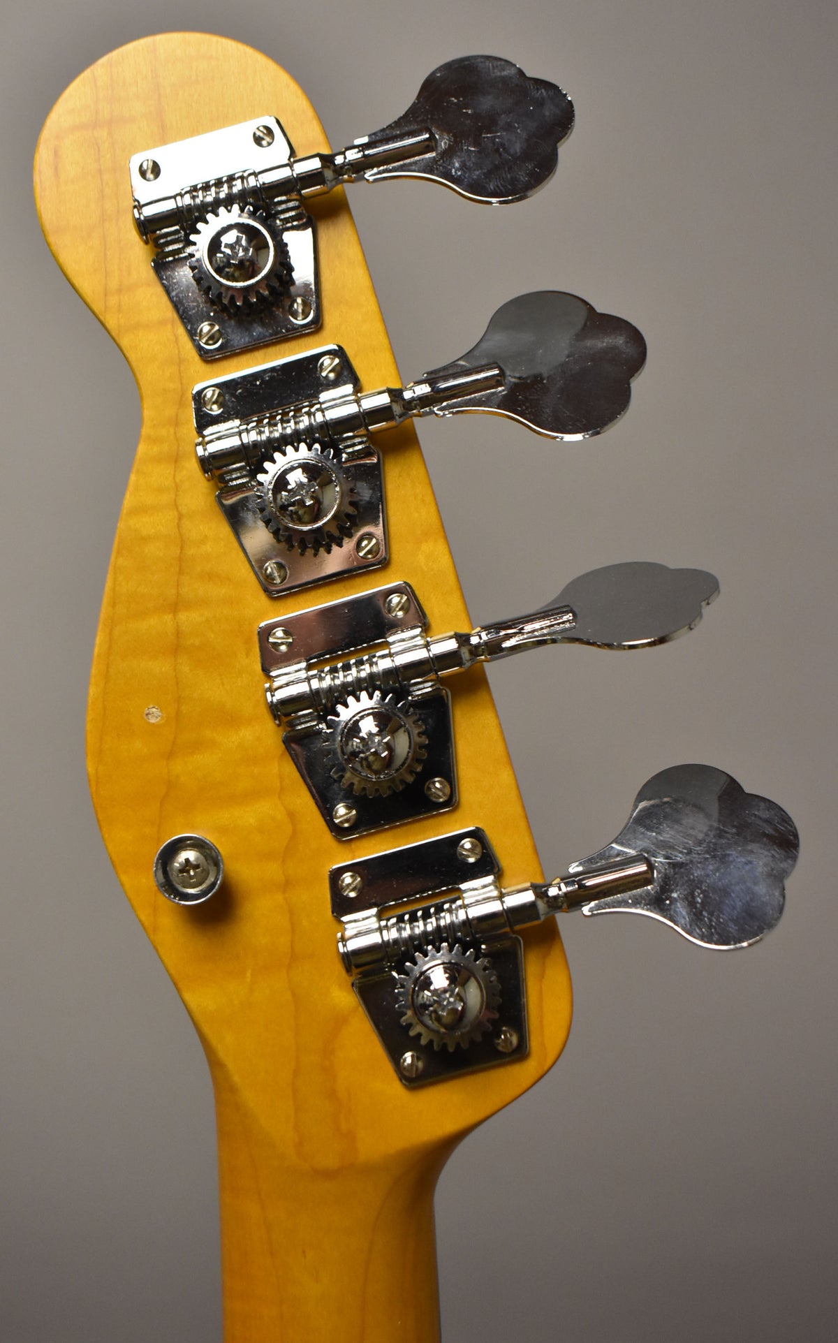 Close-up of the bass headstock, showing four chrome clover-leaf tuners on a honey-blonde maple neck with light wear.