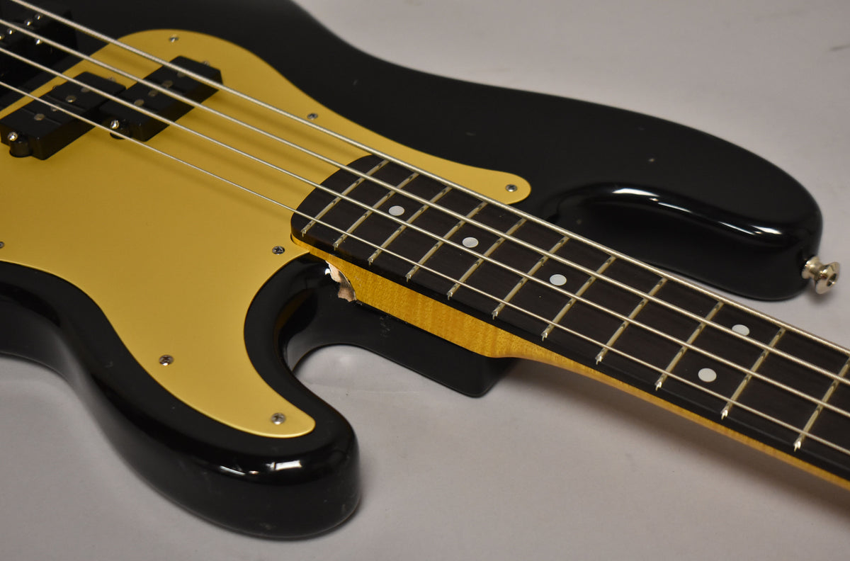 The black bass with a gold pickguard is angled from the lower bout, showing the maple neck and rosewood fretboard.