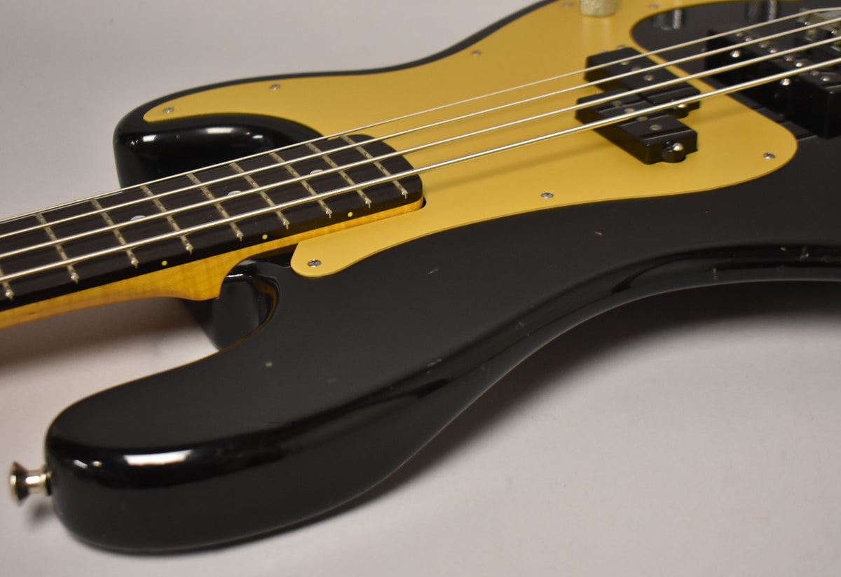 Close-up of a black bass body with a gold pickguard, showing a PJ pickup configuration and some minor finish wear.