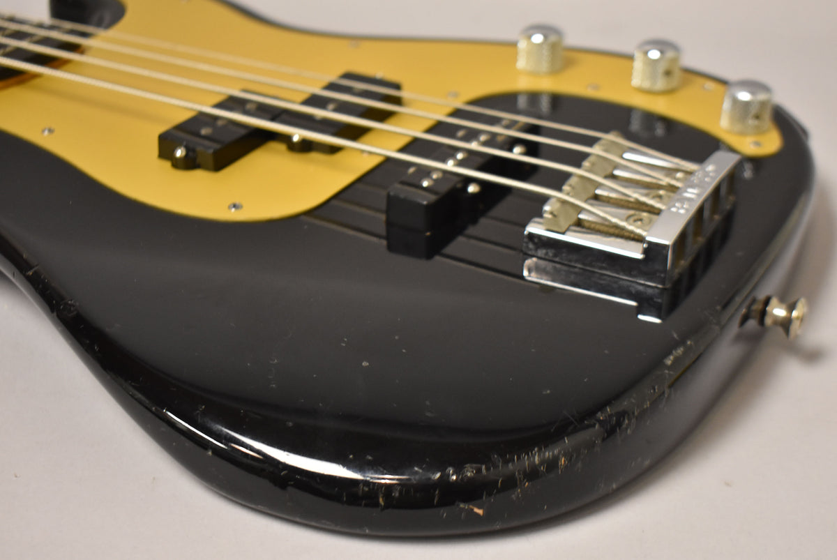 Close-up of the black bass body with a gold pickguard, showing a chrome bridge, two pickups, and heavy wear on the lower bout.