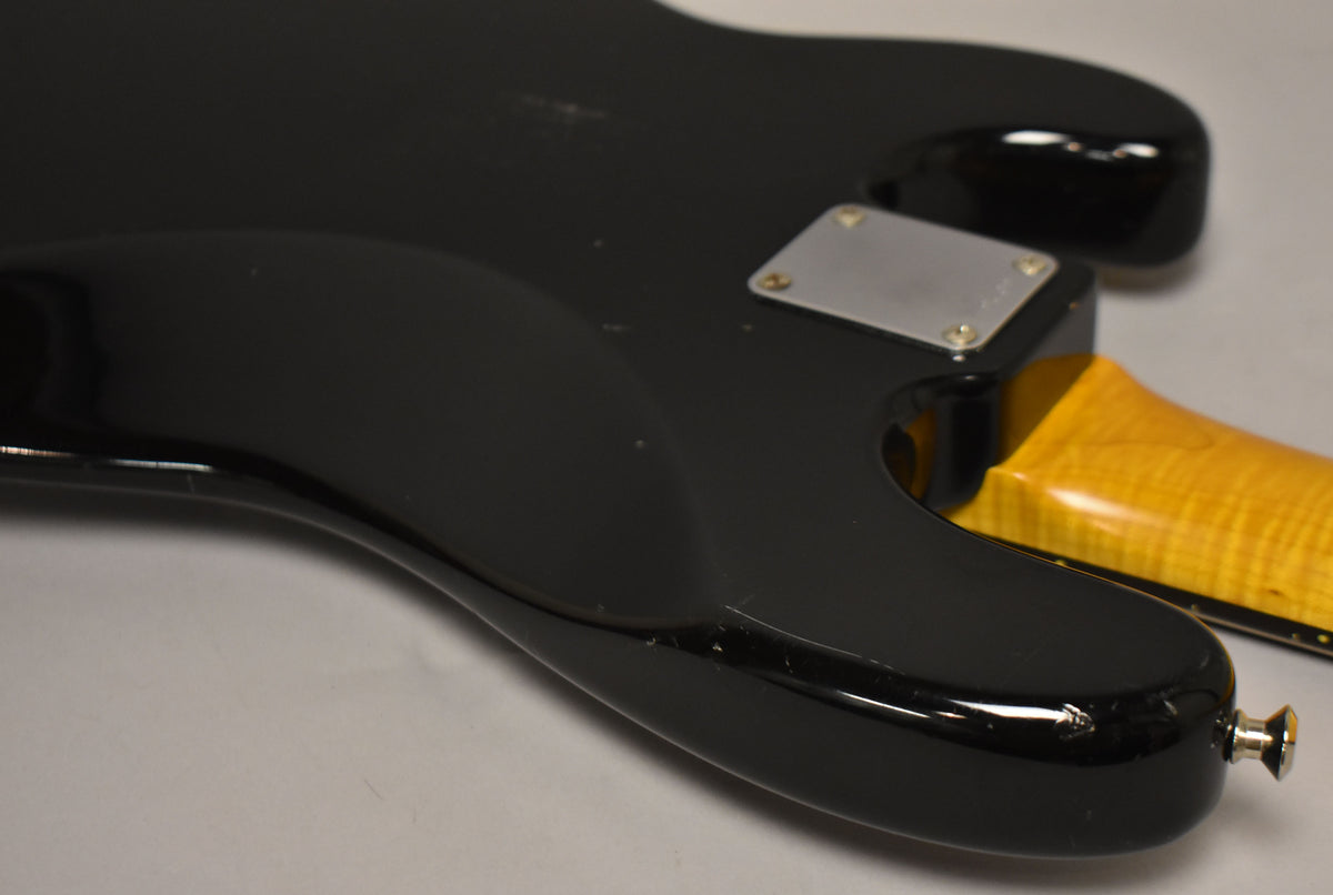 The lower horn and bottom edge of a black gloss bass body, showing a chrome strap button and a maple neck joint.