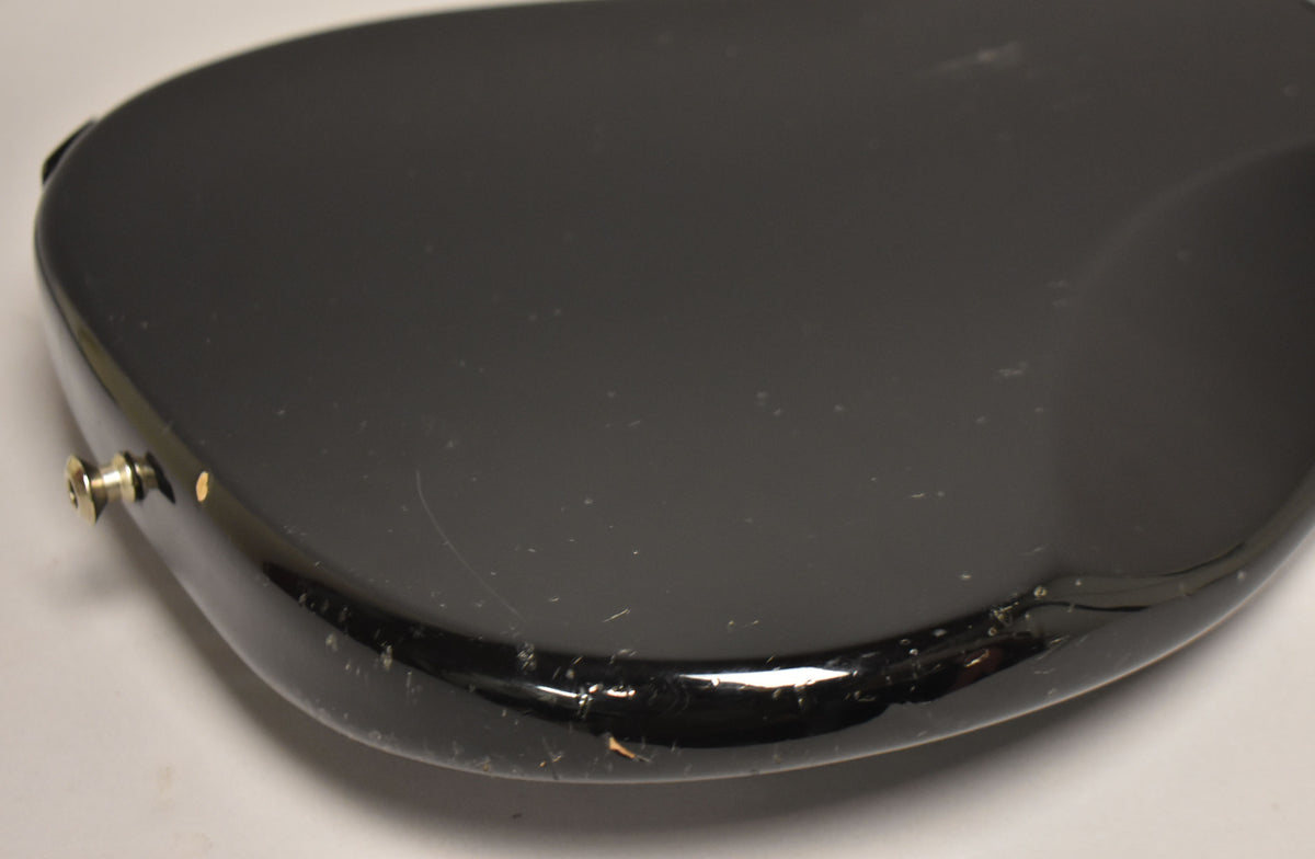 Close-up of the lower bout of a black bass body, showing many small scratches and chips in the glossy finish, and a gold strap button.