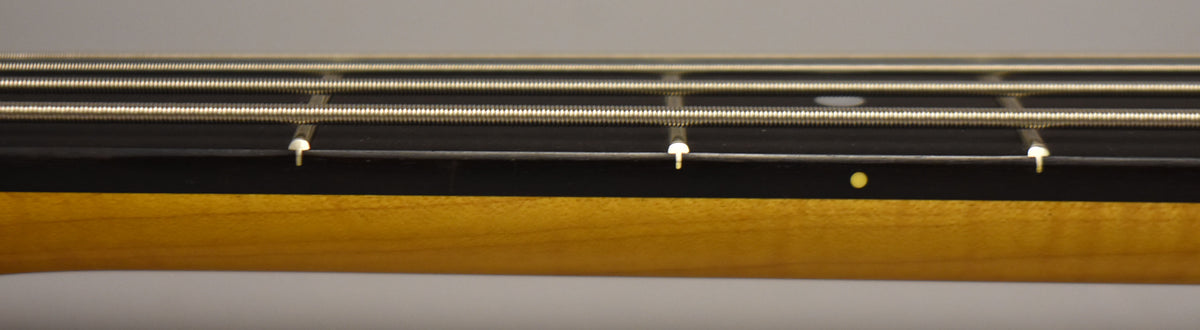 Close-up of the bass neck, showing the dark fretboard, four strings, and a single yellow dot inlay on the side.